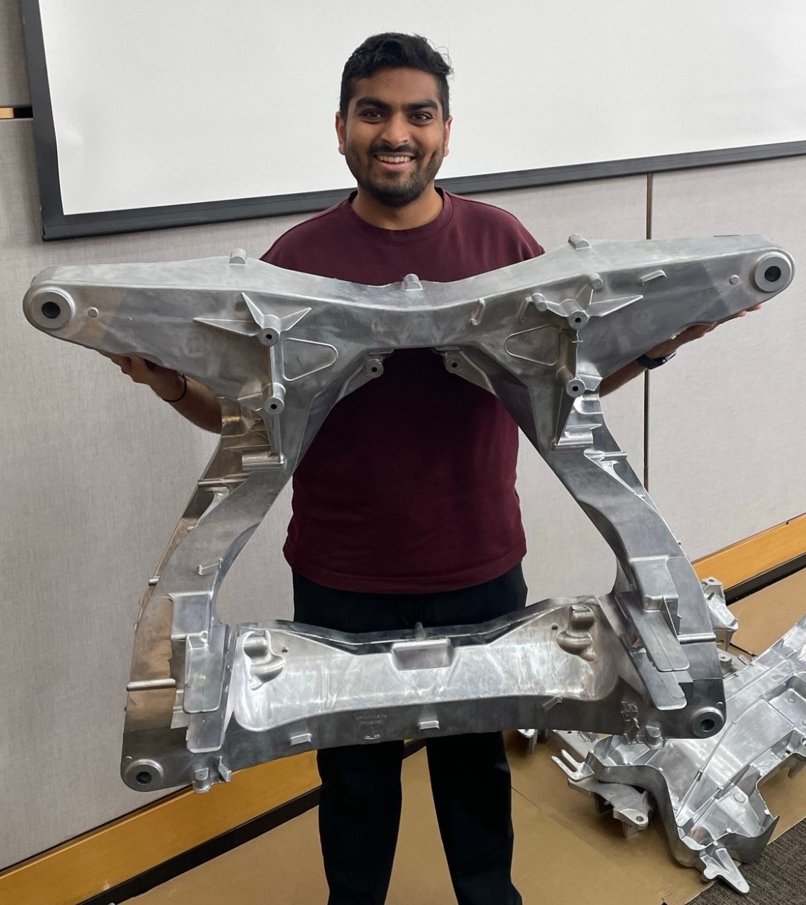 Viyat holding a single-piece high-pressure die cast aluminium rear subframe, roughly the width of his outstretched arms.
